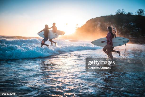 amigos corriendo en el océano con sus tablas de surf - playa amigos fotografías e imágenes de stock