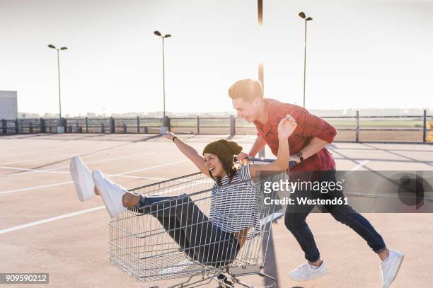 playful young couple with shopping cart on parking level - summer press day ストックフォトと画像
