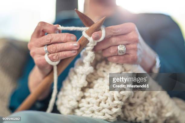 senior woman knitting on couch at home - stricknadel stock-fotos und bilder