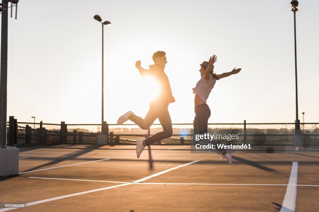 Carefree young couple jumping on parking levelat sunset