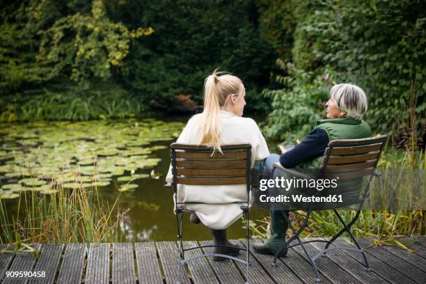 young woman with her grandmother sitting on jetty at garden pond - young woman with grandmother stock pictures, royalty-free photos & images