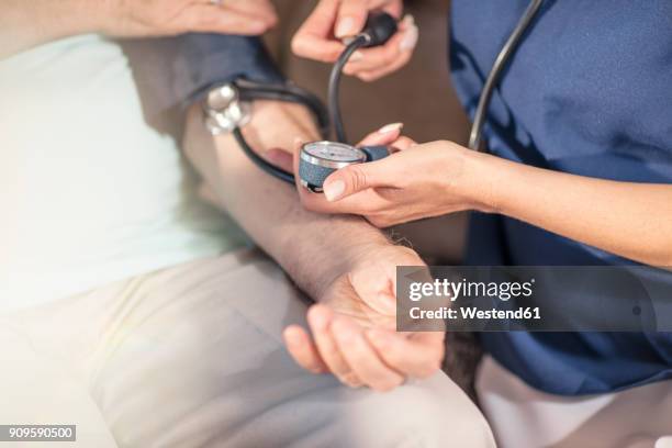 nurse taking blood pressure of senior patient at home - hypertension stock-fotos und bilder