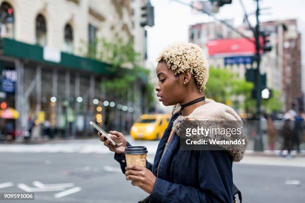 usa, new york city, fashionable young woman with coffee to go looking at cell phone on the street - beautiful woman on the street of new york city stock-fotos und bilder