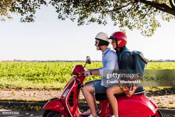 happy young couple riding motor scooter with backpack on the back - casco de deportes fotografías e imágenes de stock