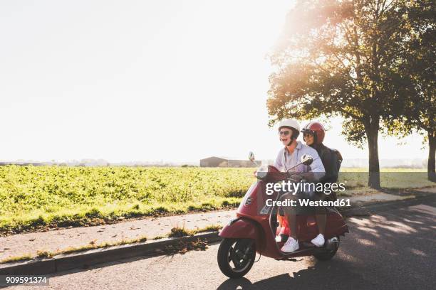 happy young couple riding motor scooter on country road - motorino foto e immagini stock