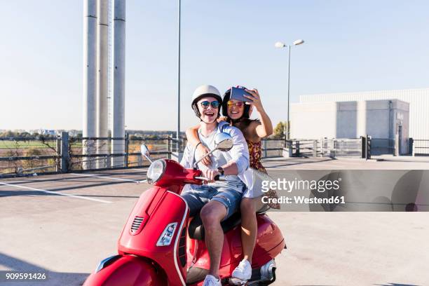 happy young couple taking a selfie on motor scooter on parking level - holiday scooter stock-fotos und bilder