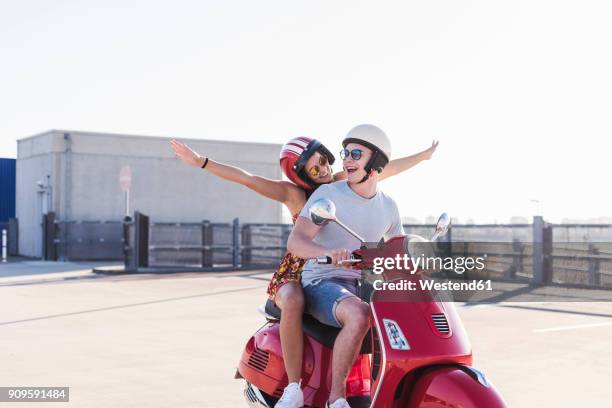 carefree young couple riding motor scooter on parking level - holiday scooter stock-fotos und bilder