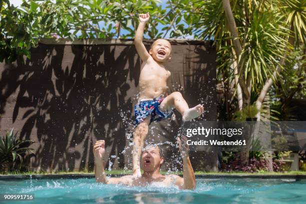 father and son having fun in swimming pool - kids fun indonesia stock-fotos und bilder