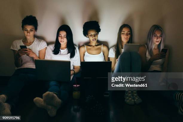 group of female friends at home sitting on floor using technology in the dark - chatting serious stock-fotos und bilder