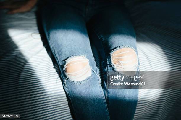 close-up of woman sitting on bed at home wearing ripped jeans - zerrissene jeans stock-fotos und bilder