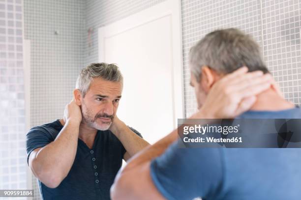 mature man looking in bathroom mirror - graues haar stock-fotos und bilder