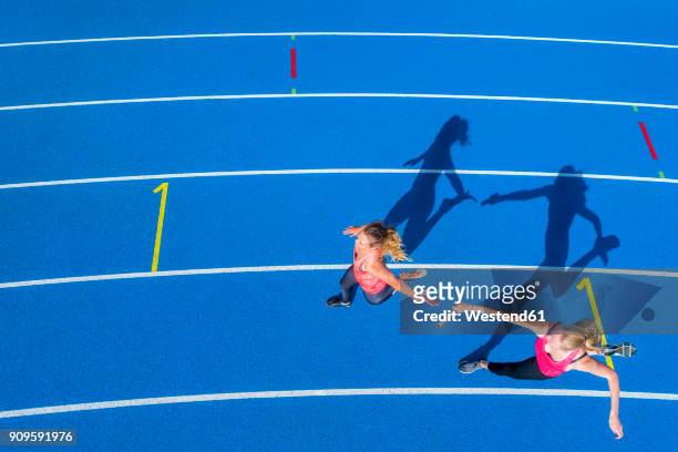 top view of two female runners passing the baton on tartan track - match sport stockfoto's en -beelden