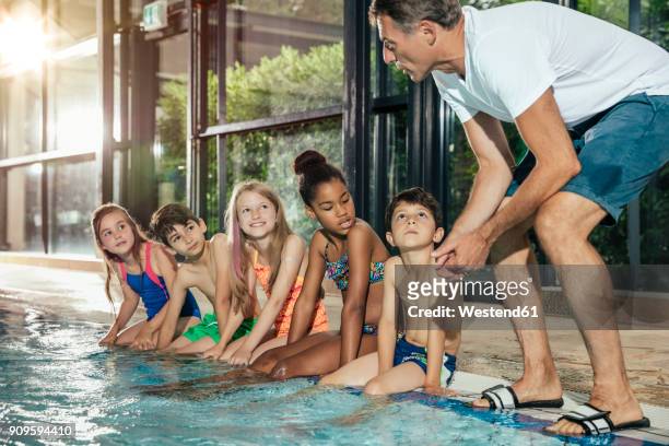 instructor talking to children sitting on poolside in indoor swimming pool - learning to swim stock-fotos und bilder