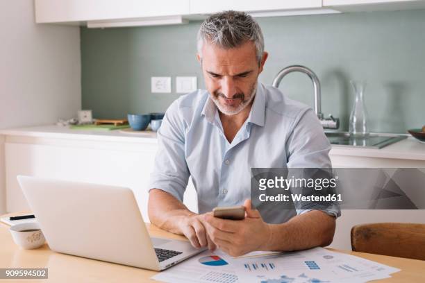 man analysing data and using laptop and cell phone in home office - white smart phone stock pictures, royalty-free photos & images