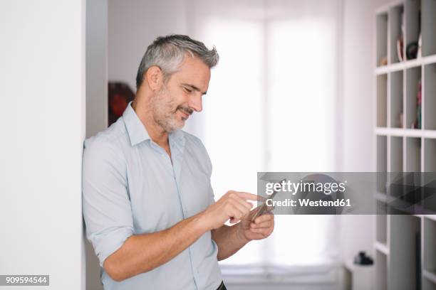 smiling mature man using cell phone at home - man 45 stock pictures, royalty-free photos & images