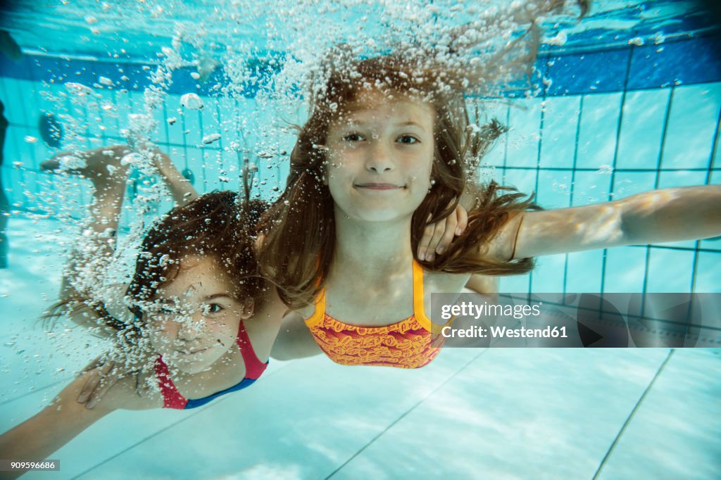 Portrait of two girls swimming under water in swimming pool