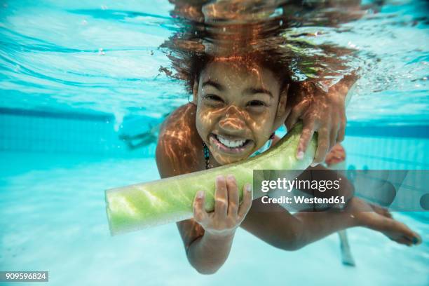 portrait of smiling girl with pool noodle under water in swimming pool - learning agility stock pictures, royalty-free photos & images