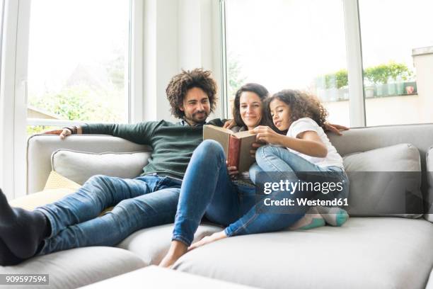 happy family sitting on couch, reading book - family oncouch stock pictures, royalty-free photos & images