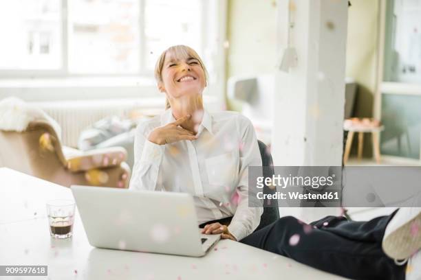 confetti falling on businesswoman with laptop in office - konzepte und themen stock-fotos und bilder