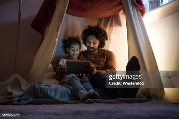 father and daughter sitting in dark children's room, looking at digital tablet - family ipad stockfoto's en -beelden