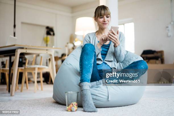 smiling woman sitting in beanbag using cell phone - online reading photos et images de collection