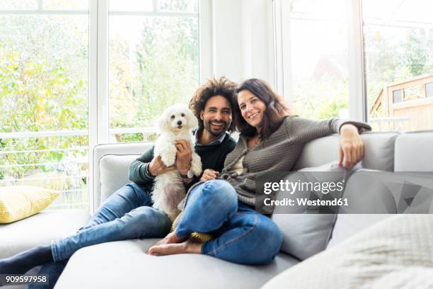 happy family with dog sitting together in cozy living room - inselrepublik malta stock-fotos und bilder