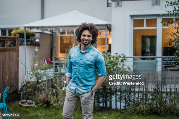 happy man standing in his garden with hands in pockets - reihenhaus stock-fotos und bilder