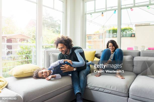happy family sitting on couch, father tickling his laughing daughter - kietelen stockfoto's en -beelden