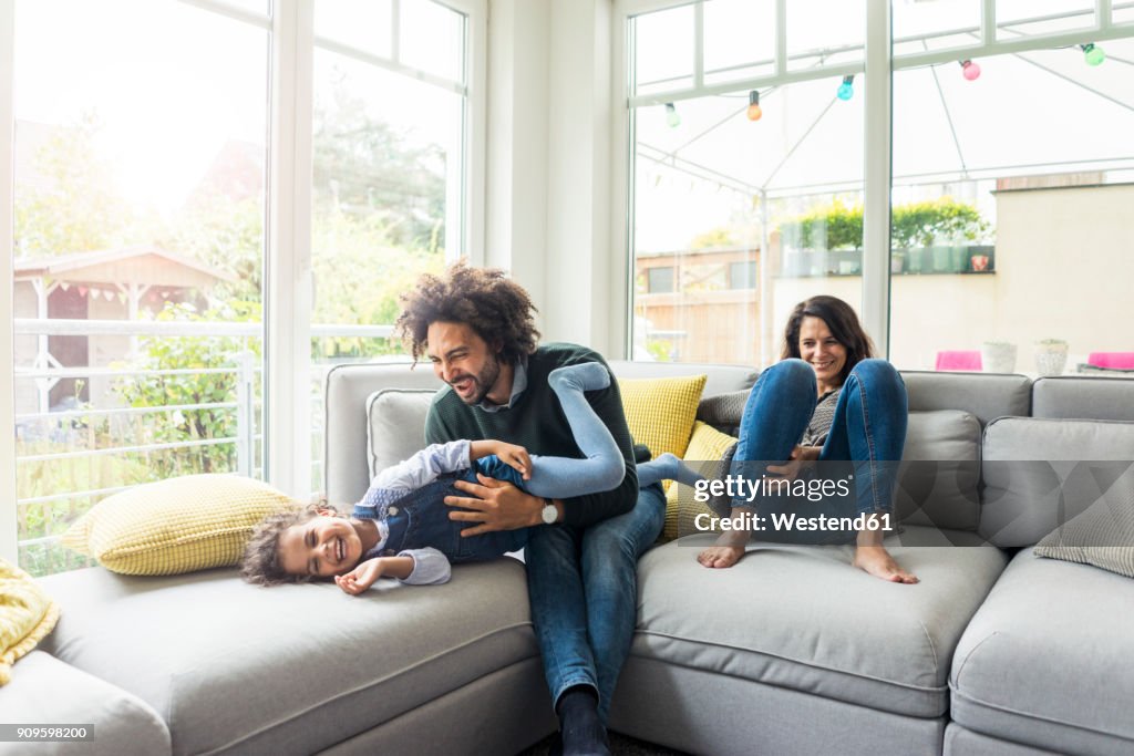 Happy family sitting on couch, father tickling his laughing daughter