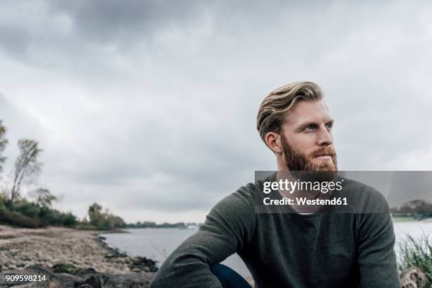 young man sitting at the river in autumn, portrait - bart stock-fotos und bilder