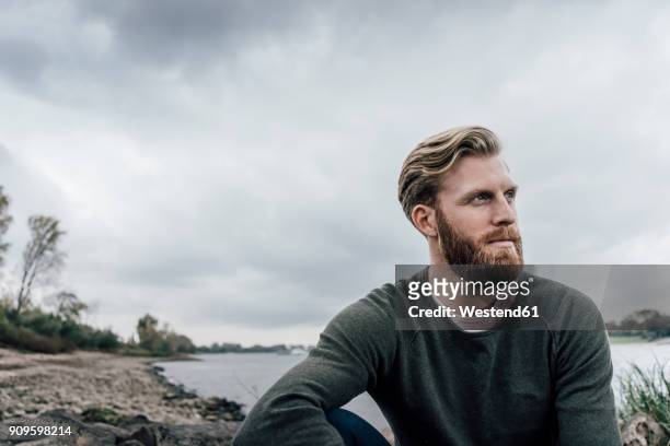 young man sitting at the river in autumn, portrait - thinking man cloud stockfoto's en -beelden