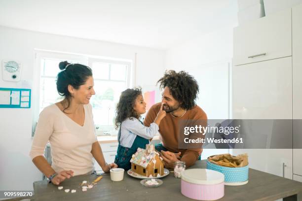 family baking gingerbread house for christmas with sweets, daughter putting icing on father's nose - kids cooking christmas photos et images de collection