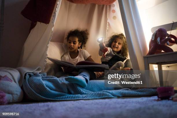 two sisters sitting in dark children's room, playing with torch, reading book - kids tent stock pictures, royalty-free photos & images