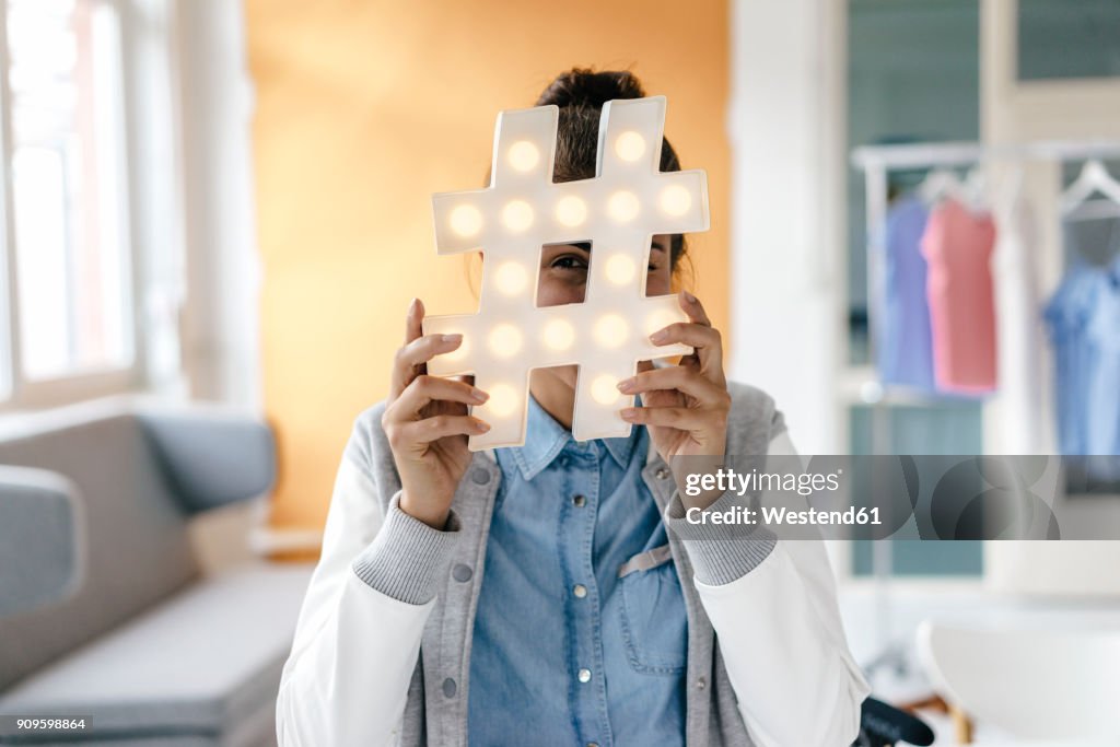 Young woman hiding behind hashtag sign in studio