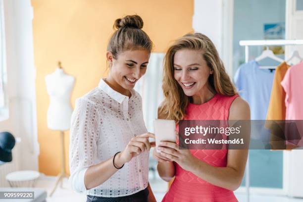 two smiling young women with cell phone in fashion studio - the girlfriend stock-fotos und bilder