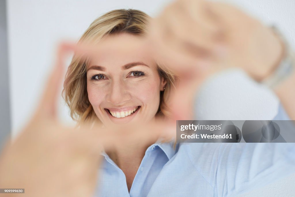 Portrait of smiling blond woman building frame with her fingers while looking at viewer