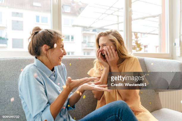 two carefree young women sitting on couch - party inside stockfoto's en -beelden