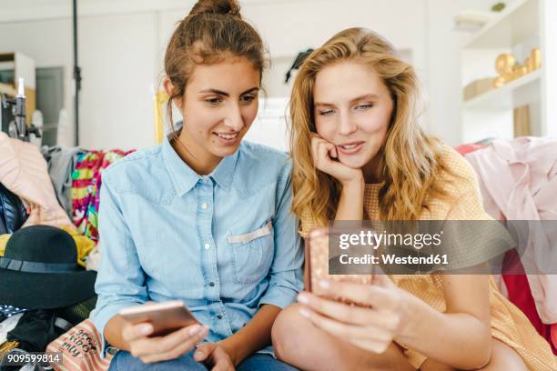 two young women sitting on couch using cell phones surrounded by fashion - fashion blogger stock pictures, royalty-free photos & images