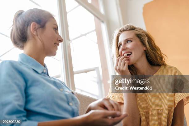 two young women sitting on couch talking - gossip foto e immagini stock