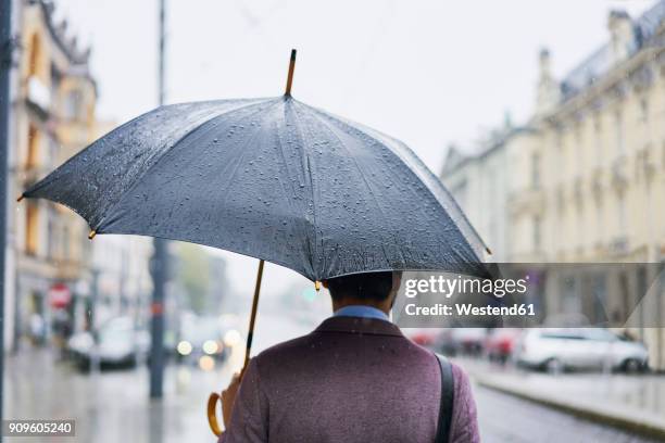 back view of businessman in the city with umbrella on a rainy day - umbrella rain stock-fotos und bilder