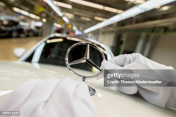 An employee mounts a Daimler AG Mercedes-Benz emblem to the hood of a S-Class sedans at the Mercedes-Benz plant on January 24, 2018 in Sindelfingen,...