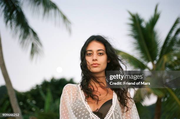 tan young woman on tropical beach looks confidently at the camera - dom tom photos et images de collection