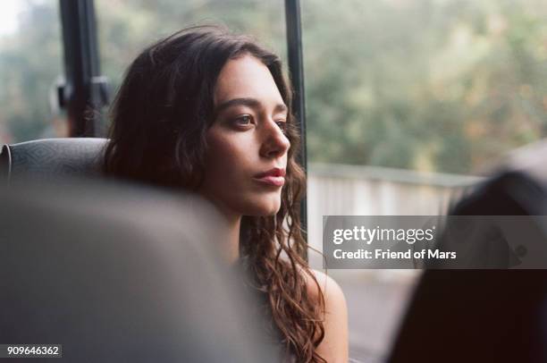 a young woman rides a bus and stares serenely out the window - bus imagens e fotografias de stock