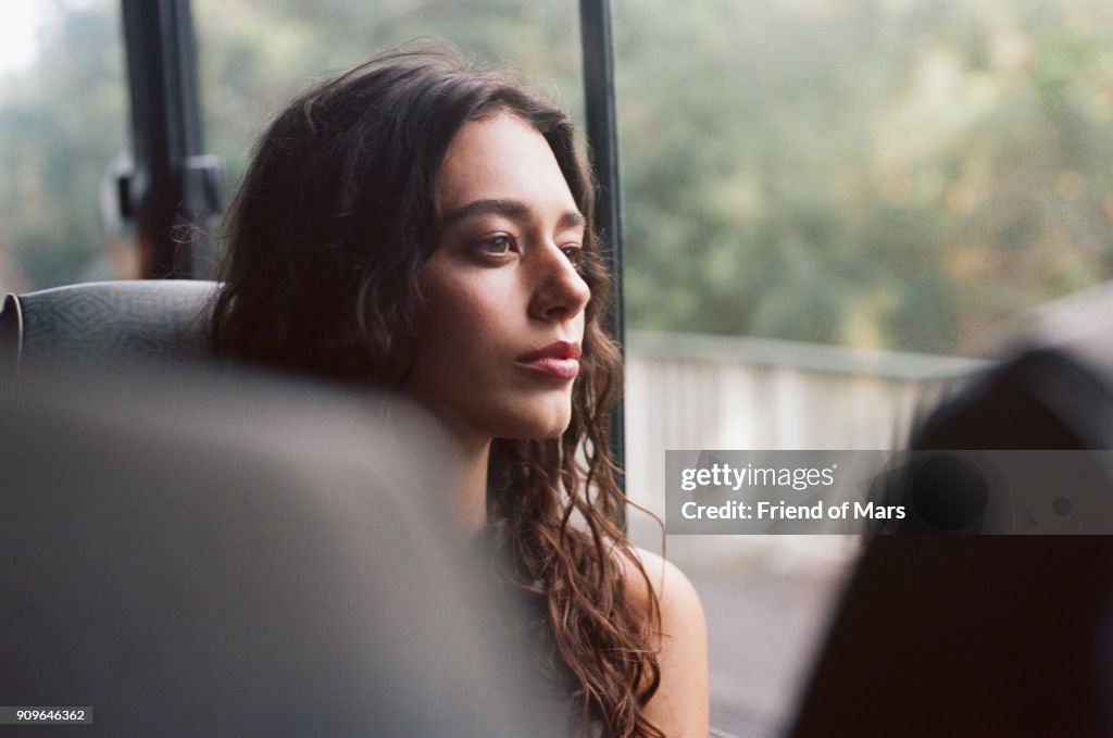 A young woman rides a bus and stares serenely out the window