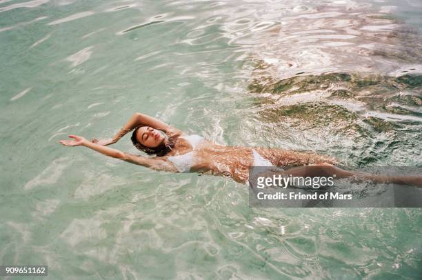 young brunette woman in white bikini swims peacefully in the ocean - pretty brunette woman fotografías e imágenes de stock
