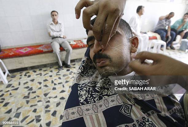 An Iraqi man has facial hair removed using string at a barbers shop on September 19 in central Baghdad, as people begin to prepare for the up coming...