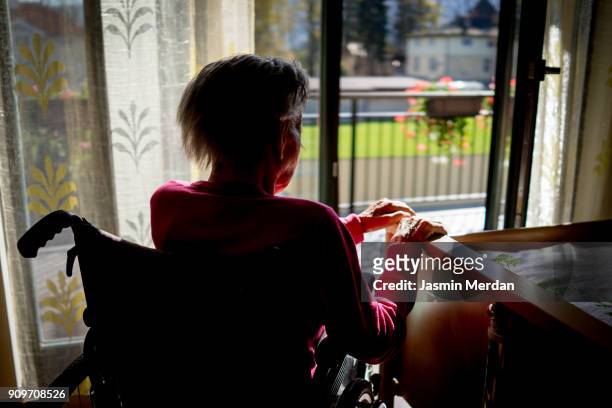 disabled senior woman in wheelchair at home in living room - memory loss stockfoto's en -beelden