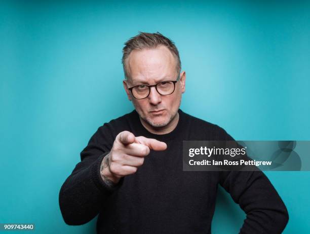 portrait of middle-aged man on blue background pointing - finger pointing stock-fotos und bilder