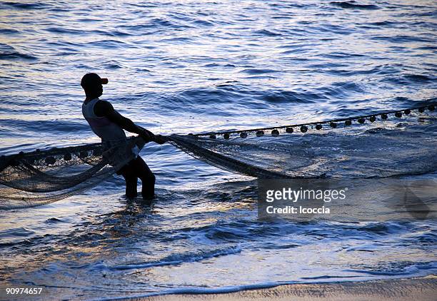 a silhouette of a fisherman pulling a net in the surf - sierra leone beach stock pictures, royalty-free photos & images