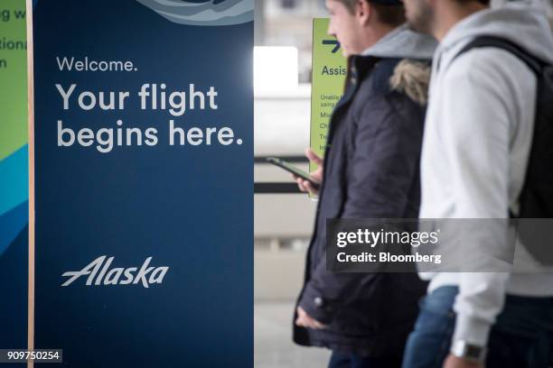 Travelers pass in front of Alaska Air Group Inc. Signage at the San Francisco International Airport in San Francisco, California, U.S., on Friday,...